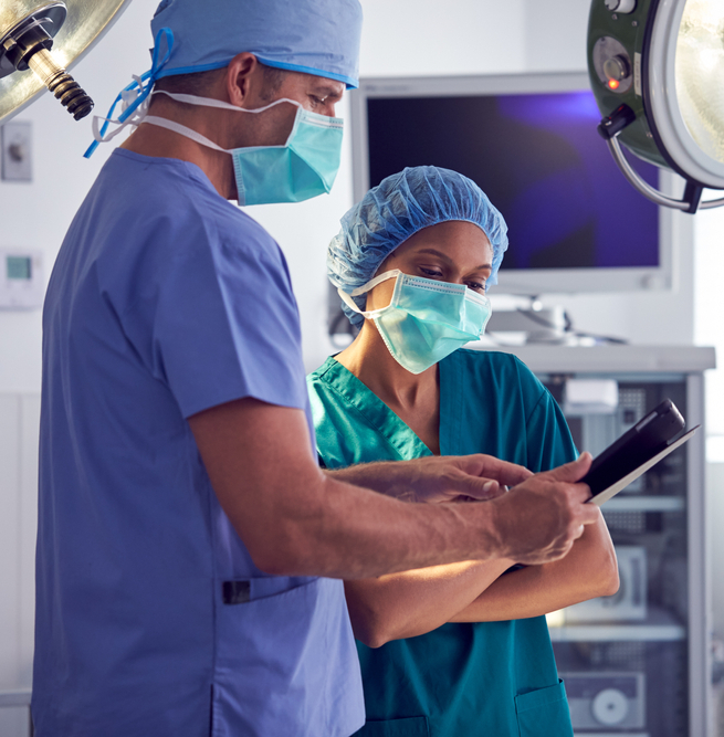 Male,And,Female,Surgeons,Wearing,Scrubs,Looking,At,Digital,Tablet